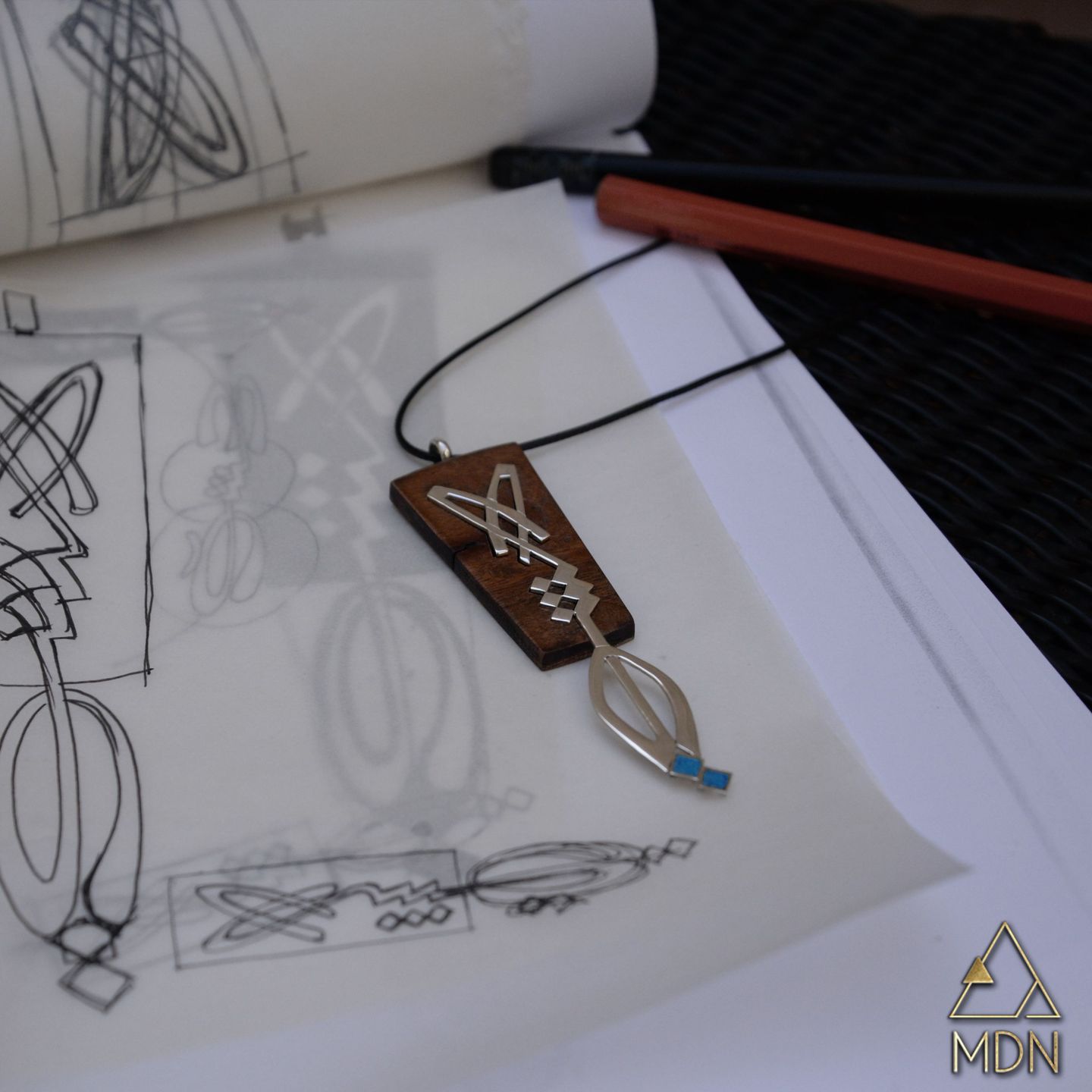 Wooden rectangular pendant with geometric pattern on cord, shown with design sketches.