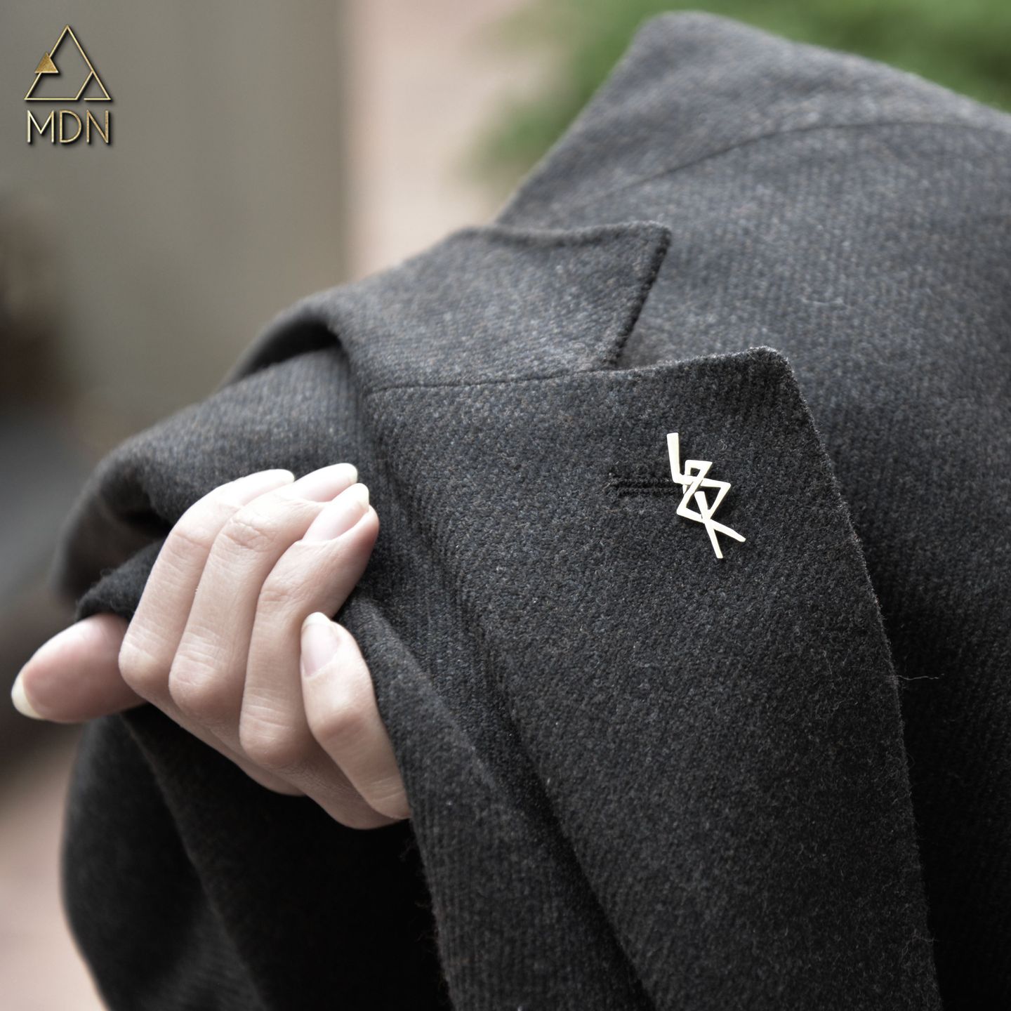 Geometric pin with calligraphy pattern worn on dark jacket.