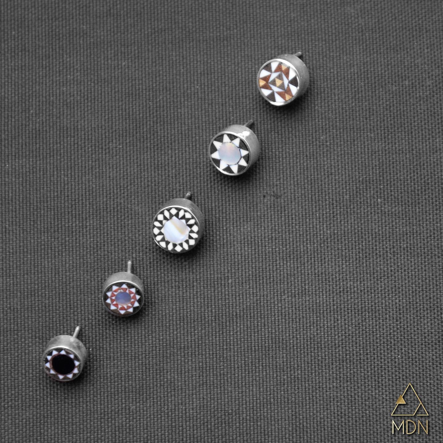 Five mosaic pins in graduating sizes with geometric inlay patterns.