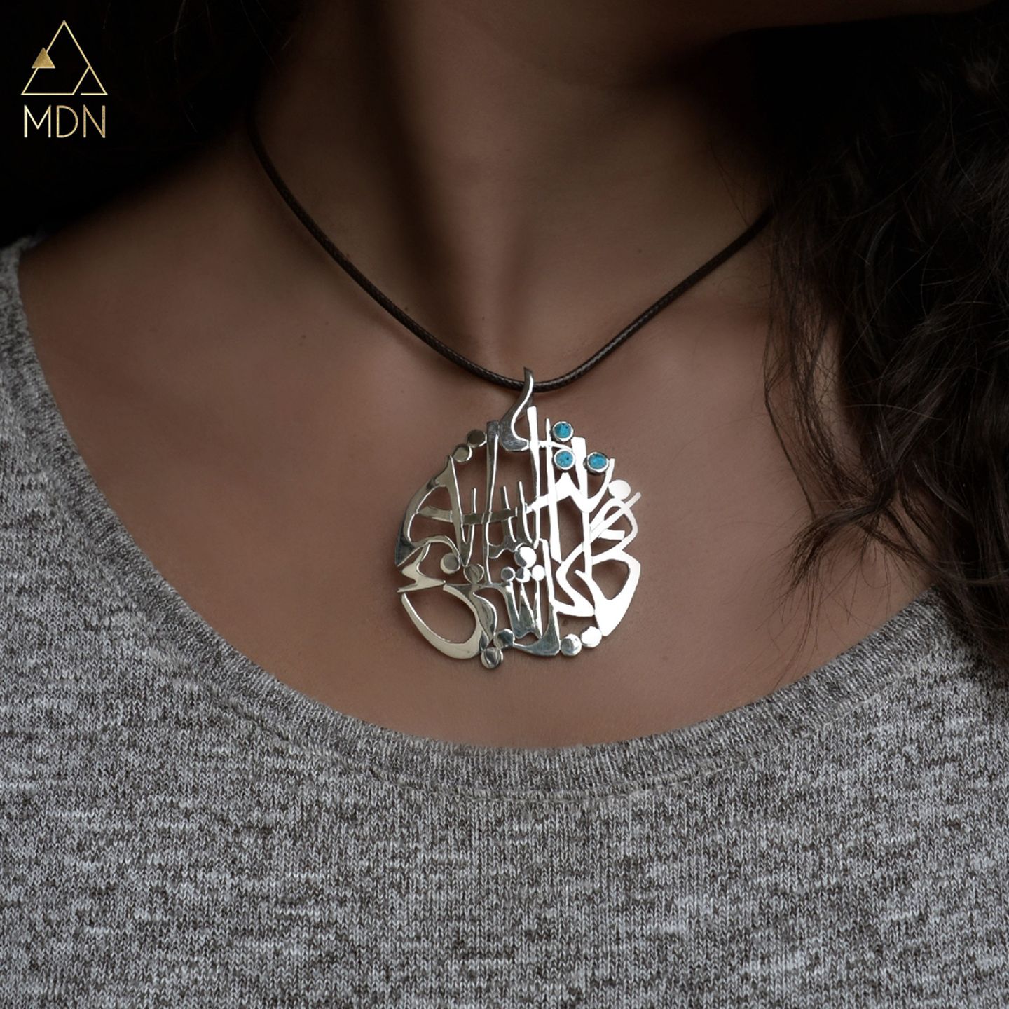 Pendant with Arabic calligraphy "انت البداية في كل شيء" worn on person.