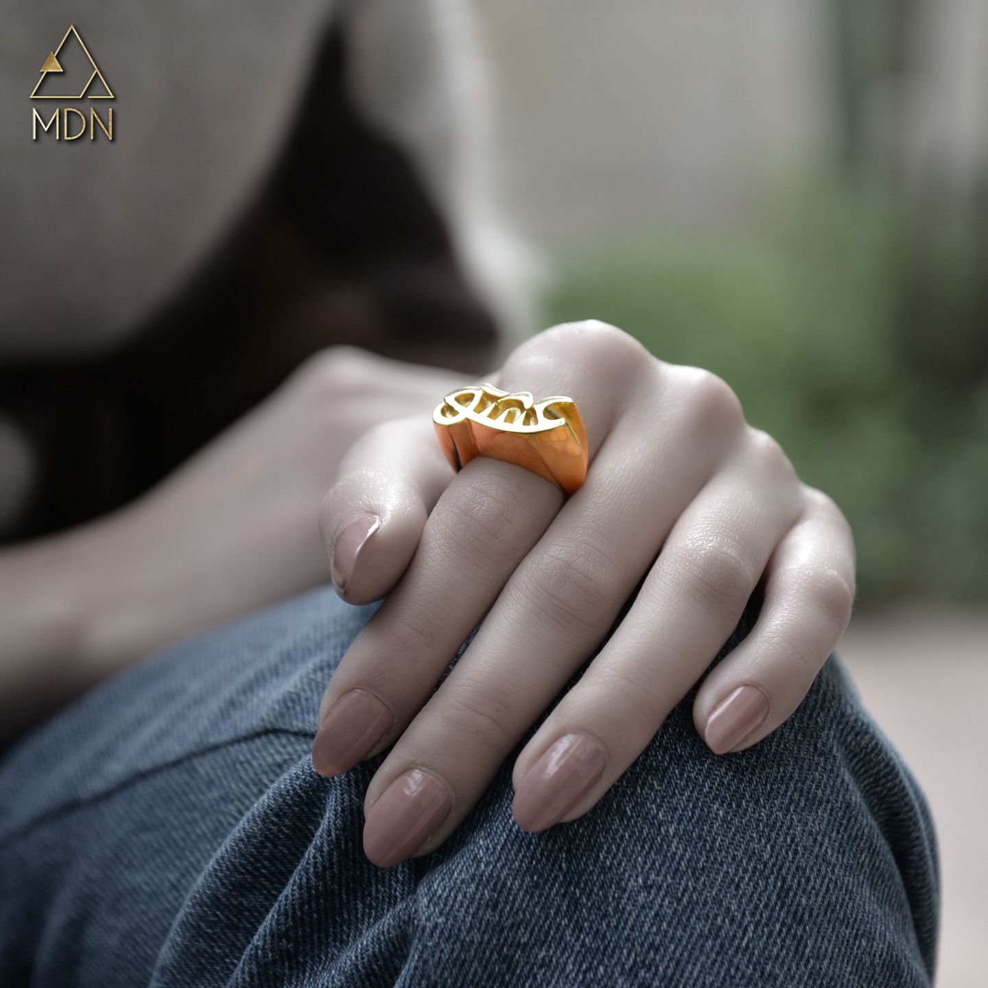 Gold-toned ring with flowing geometric pattern reading "عشق" worn on hand.