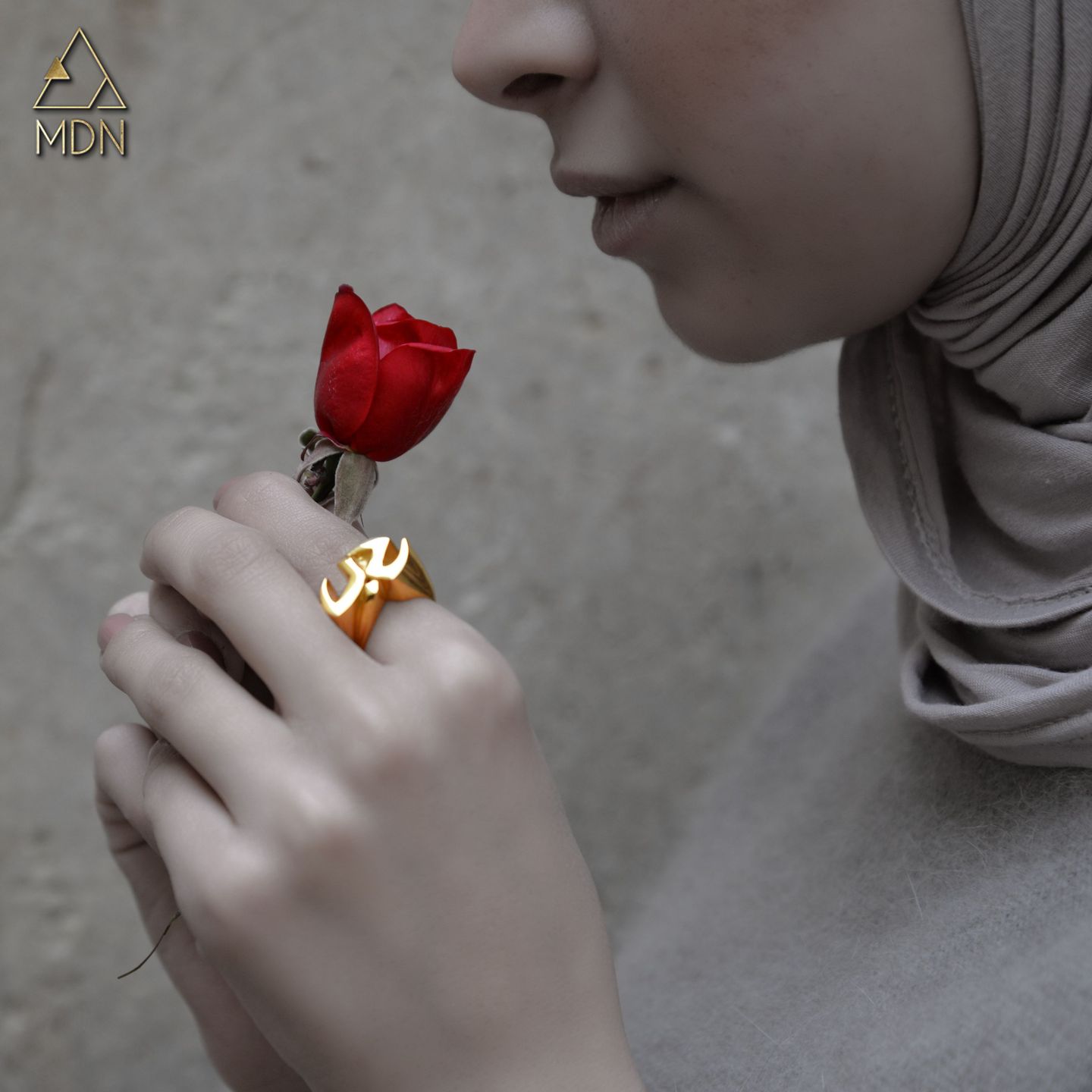 Gold-toned ring carrying Arabic calligraphy reading "حب" worn alongside red rose.