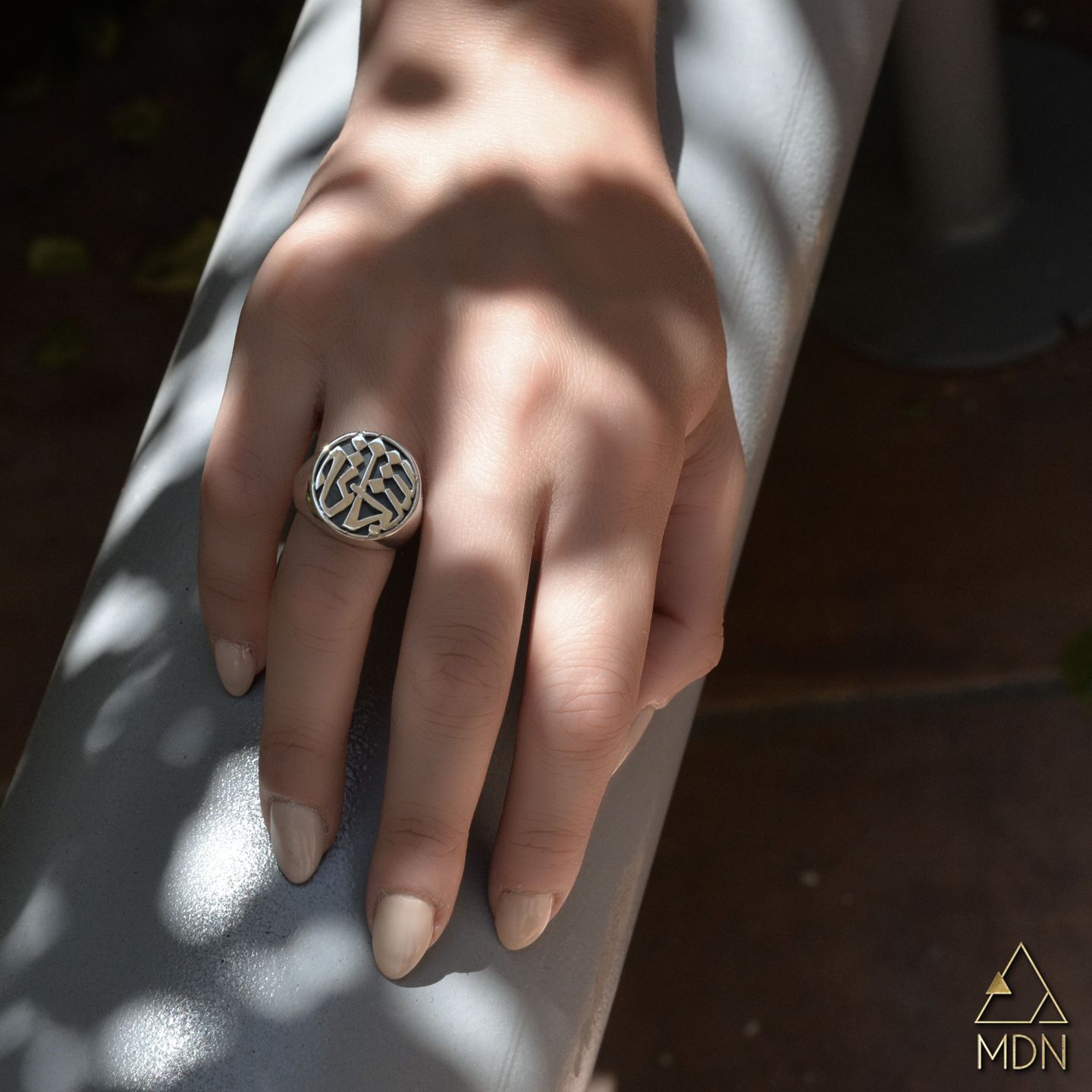 Ring with circular geometric calligraphy pattern reading "شجاعة" worn on hand.